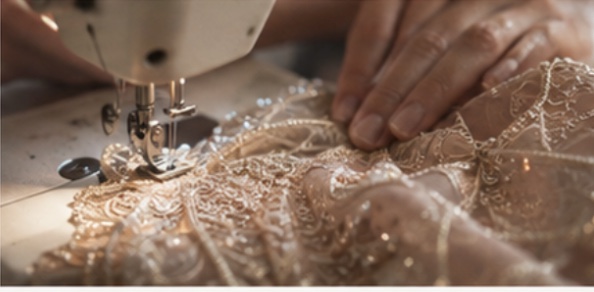 Hands guiding beaded lace fabric through a sewing machine